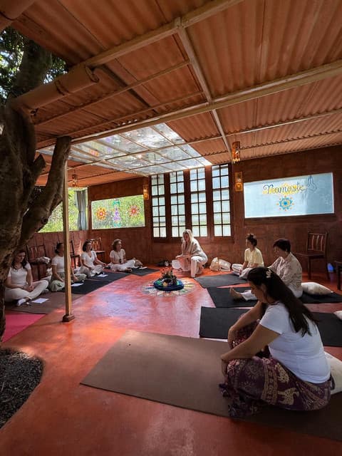 Turma reunida em círculo, sentada no chão de um espaço aberto de madeira, durante uma vivência